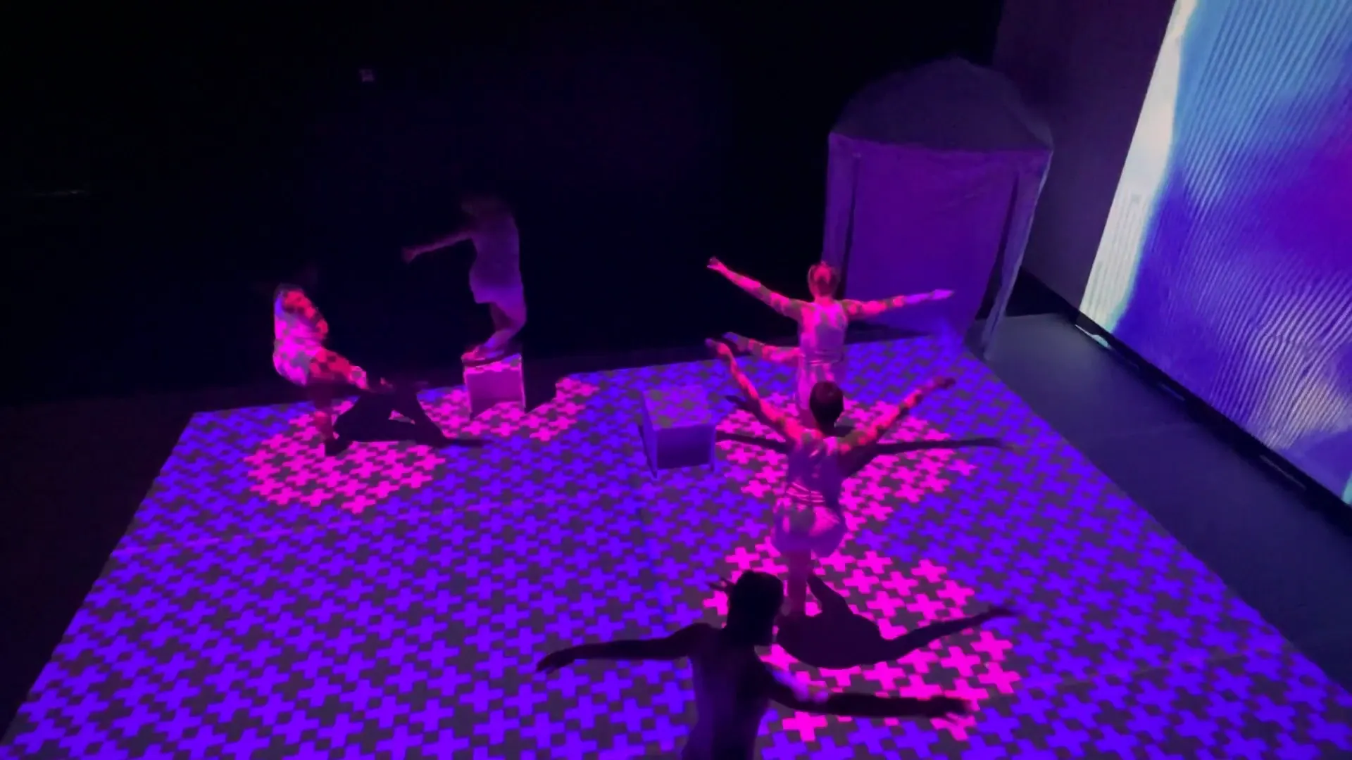Performers on a floor covered in magenta projected patterns.