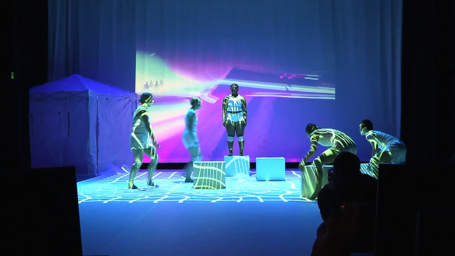 Performers onstage in front of colorful projected graphics.